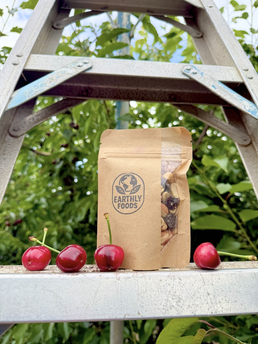 A bag of Earthly Foods trail mix on a ladder next to freshly picked cherries.
